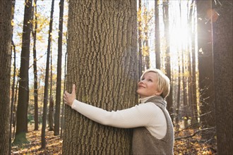 USA, New Jersey, Smiling woman hugging tree in Autumn forest. Photo : Tetra Images