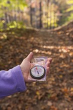 USA, New Jersey, Close-up of woman's hand holding compass in Autumn forest. Photo: Tetra Images