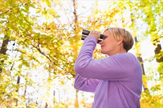 USA, New Jersey, Woman looking through binoculars in Autumn forest. Photo : Tetra Images