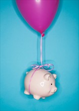 Studio shot of piggy bank lifted by balloon.