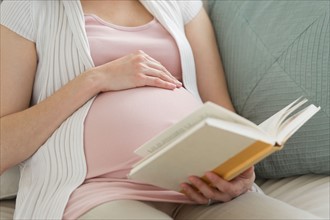 Midsection of pregnant woman reading book.