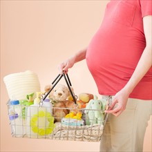 Studio shot of woman with shopping basket full of baby goods, midsection.