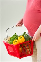 Studio shot of woman with shopping basket full of groceries, midsection.