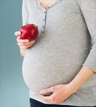 Studio shot of pregnant woman eating apple, midsection.