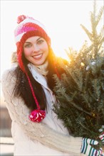 Portrait of young woman carrying Christms tree.