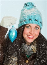 Studio portrait of woman in winter clothing holding Christmas ornament.