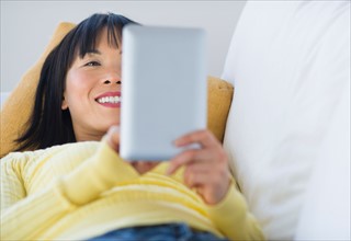 Smiling woman lying on sofa and using digital tablet.