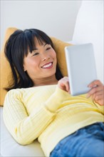 Smiling woman lying on sofa and using digital tablet.