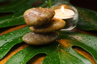 Spa stones and candle on tropical leaf, studio shot.