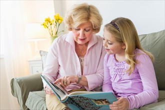 Grandmother with granddaughter (8-9) reading on sofa.