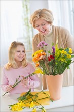 Smiling senior woman arranging flowers with granddaughter (8-9).
