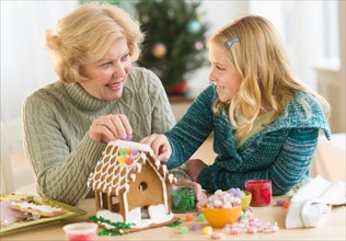 Grandmother with granddaughter (8--9) making gingerbread house.