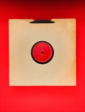Vinyl record in envelope on red background, studio shot.