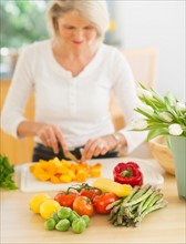 Portrait of senior woman cutting vegetables in kitchen.