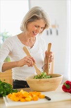 Portrait of senior woman preparing salad in kitchen.