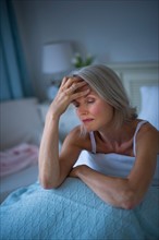 Senior woman sitting in bed and suffering from headache.
