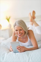 Senior woman lying on bed and using digital tablet.