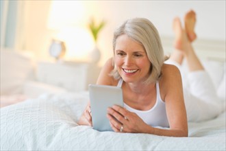 Senior woman lying on bed and using digital tablet.