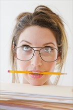Portrait of young woman wearing glasses and holding pencil in mouth, studio shot.
