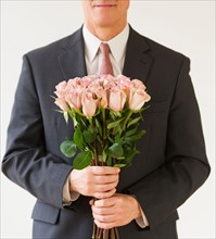 Close up of man in suit holding bouquet of roses, studio shot.