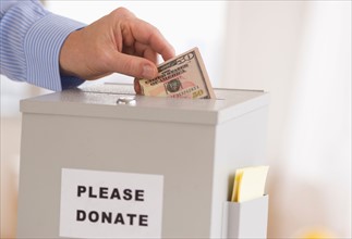 Man's hand putting dollars into donation box.