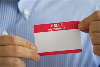 Close up of businessman's hands holding blank name tag, studio shot.