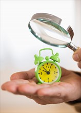 Close up of man's hand holding alarm clock and magnifying glass, studio shot.