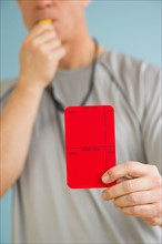 Male referee showing red card, studio shot.