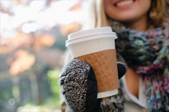 Woman wearing gloves holding coffee cup. Photo : Jamie Grill