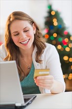 Young woman on-line shopping from home with Christmas tree on background. Photo : Daniel Grill