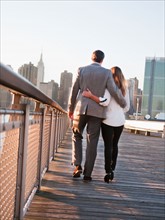 USA, New York, Long Island City, Rear view of young couple walking on boardwalk, Manhattan skyline
