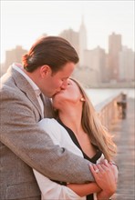 USA, New York, Long Island City, Young couple kissing on boardwalk, Manhattan skyline in background
