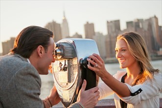 USA, New York, Long Island City, Young couple looking through coin operated binoculars, Manhattan