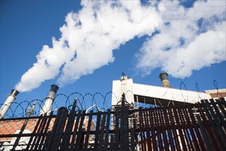 low angle view of factory chimneys behind fence. Photo : fotog