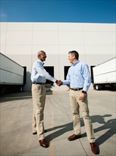 Business men shaking hands outside warehouse.