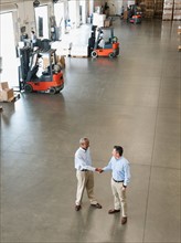 Two businessmen shaking hands in warehouse.