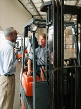 Businessman talking to forklift driver in warehouse.