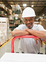 Portrait of man pushing hand truck in warehouse.