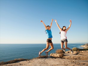 USA, California, San Diego, Two women jumping at sea coast.