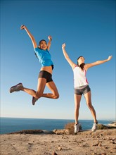 USA, California, San Diego, Two women jumping at sea coast.