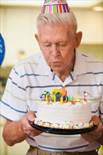 Senior man blowing candles on birthday cake.