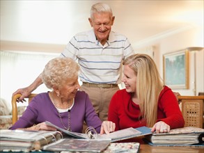 Senior couple and mid adult woman watching family scrapbooks.