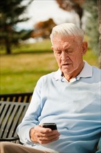 Senior man using phone in park.