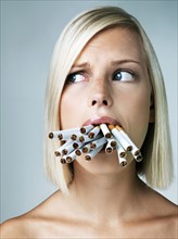 Studio portrait of young woman with mouthful of cigarettes. Photo : Yuri Arcurs