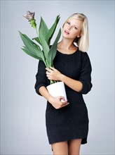 Young woman holding flowering plant, studio shot. Photo : Yuri Arcurs