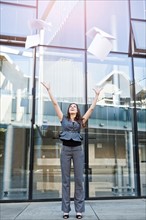 USA, Seattle, Young businesswoman throwing documents in front of office building. Photo : Take A