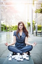 USA, Seattle, Young businesswoman meditating in front of crumbled paper balls. Photo : Take A Pix