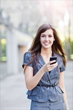 Young elegant woman standing and using mobile phone. Photo : Take A Pix Media
