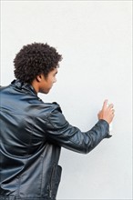 Man holding spray paint against white wall, studio shot. Photo : Sarah M. Golonka