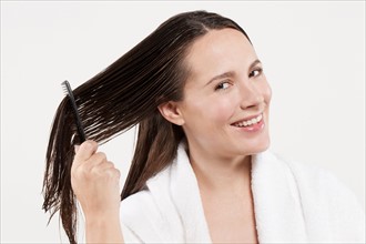 Portrait of woman combing wet hair, studio shot. Photo : Jan Scherders